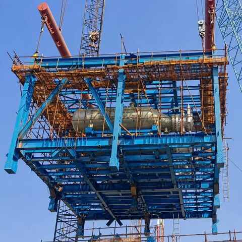 Steel structure platform under construction with cranes, scaffolding, and elevated industrial framing.